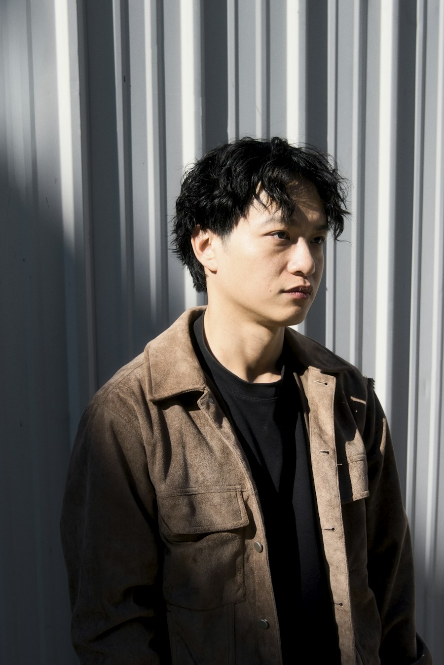 Man in brown jacket stands against corrugated wall