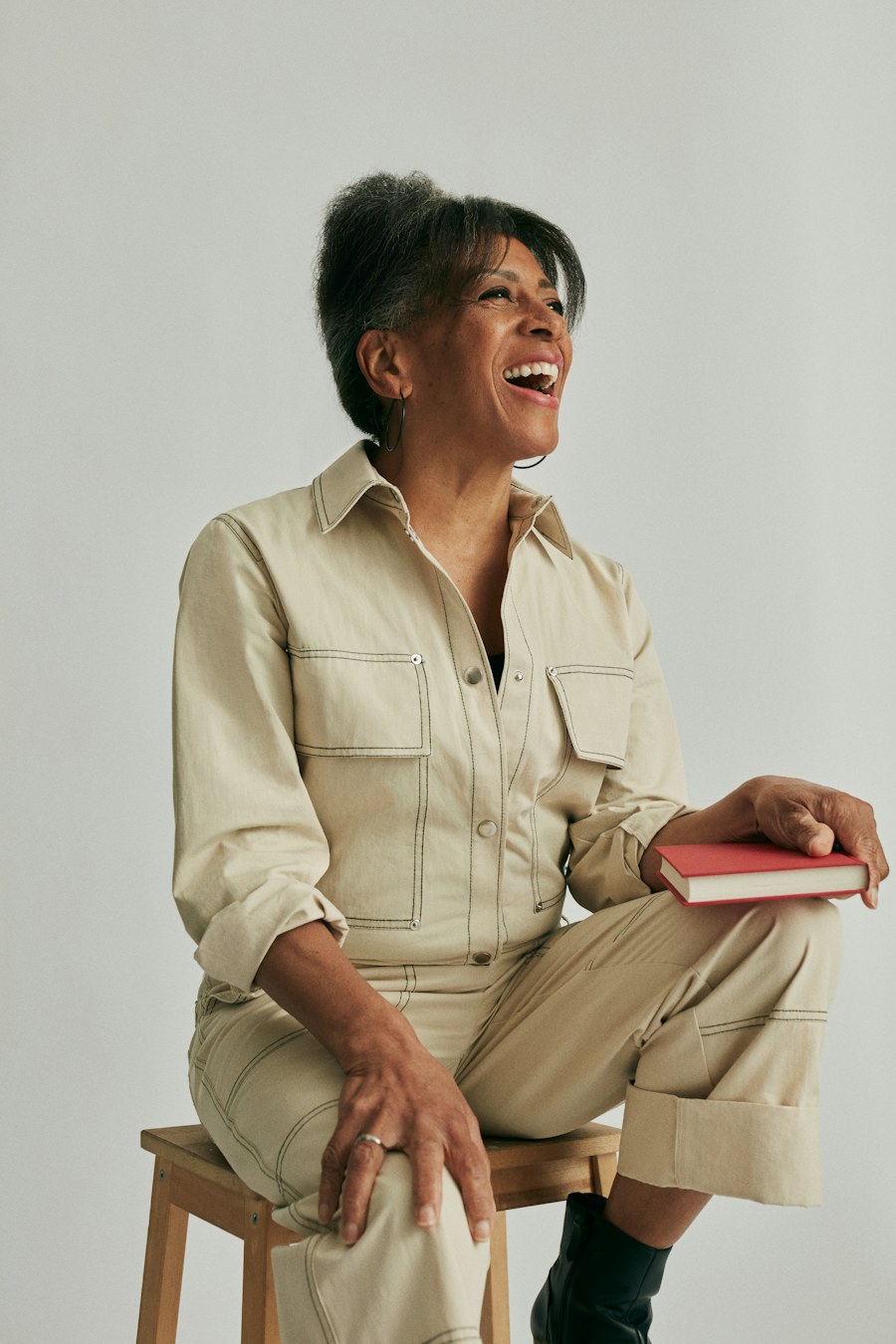 A laughing woman in a jumpsuit holds a red book