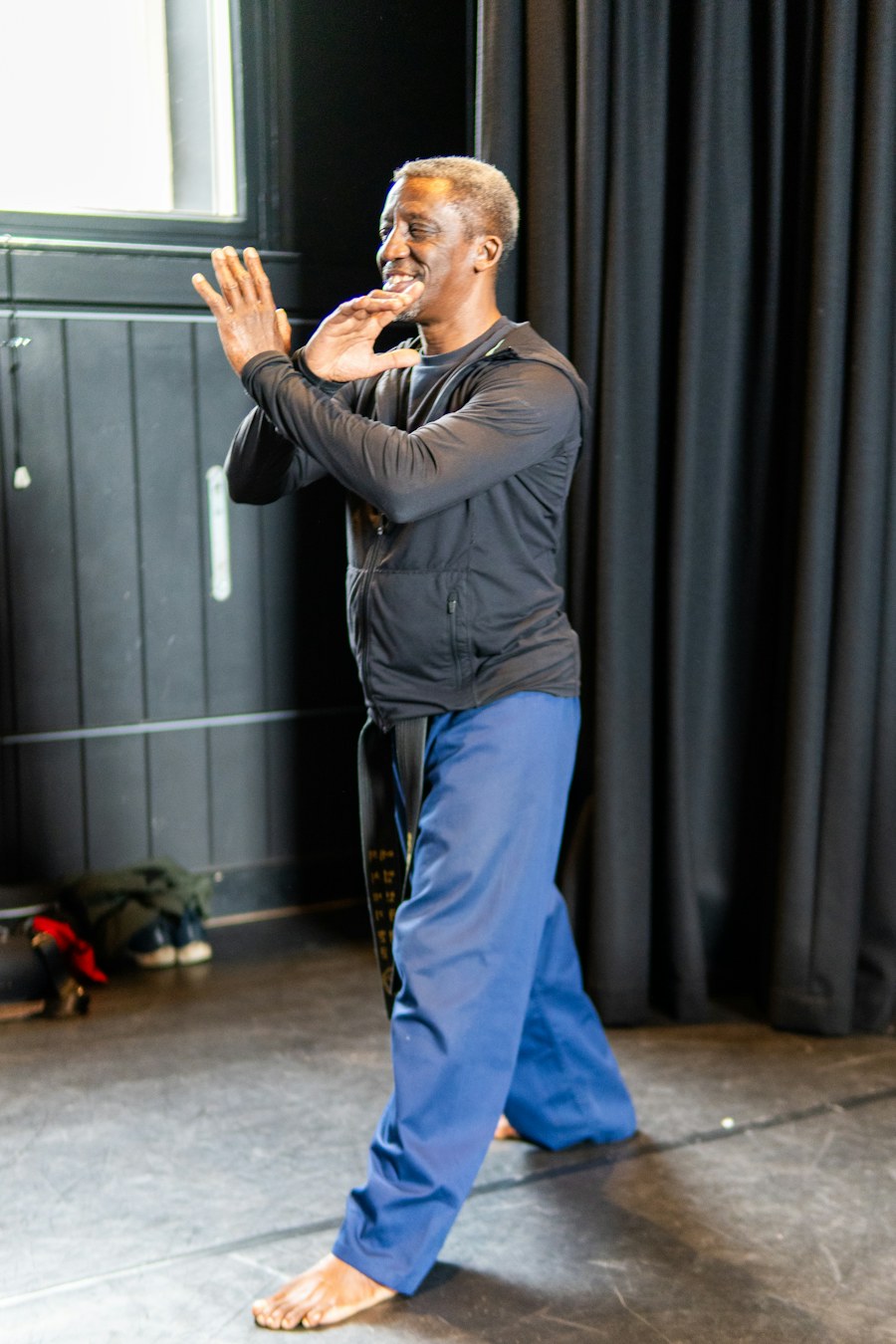 A man in a black jacket and blue pants practicing martial arts barefoot